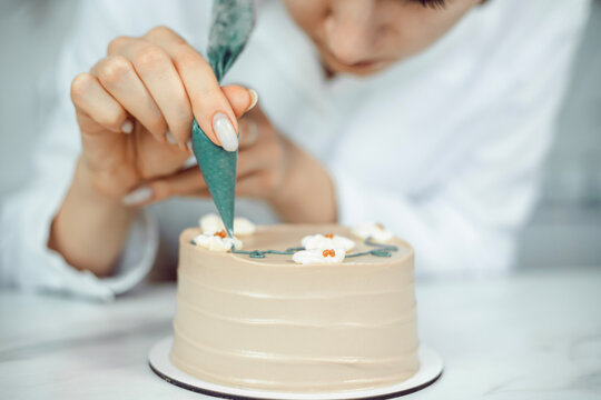 Confectioner decorates cake with icing in a kitchen setting during daylight hours