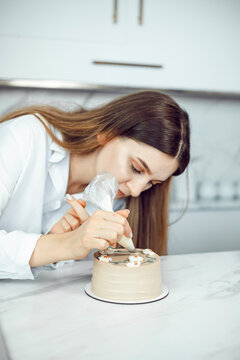 Confectioner decorates cake with icing in a kitchen setting during daylight hours