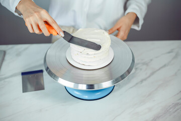 Confectioner prepares a cake with frosting on a rotating cake stand in a kitchen space during daylight hours