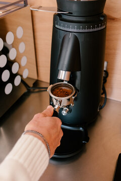 Man&rsquo;s hand holding a coffee filter holder under modern coffee grinder
