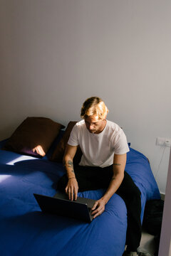 Young man working from home, sitting on the edge of a bed 