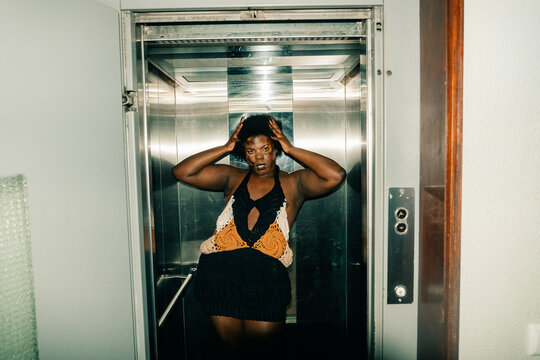 Person Poses in an Elevator Wearing Black and Orange Outfit