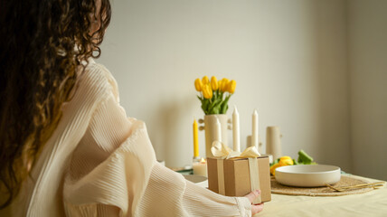 Fototapeta premium Woman holding a gift box with a ribbon on a table with tulips and candles