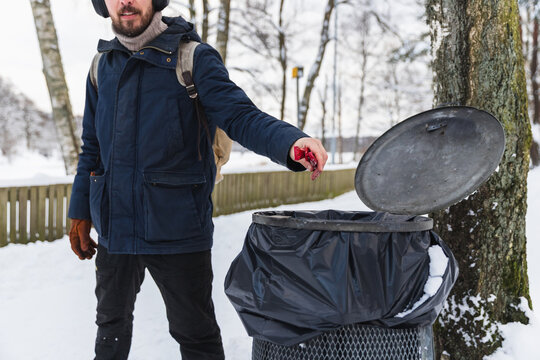 Responsible hiker throwing trash in bin in snowy winter park