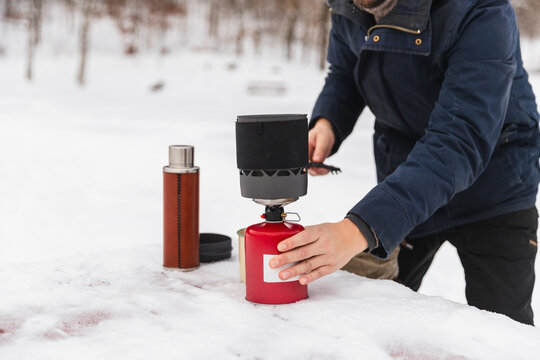 Man preparing hot coffee with camping stove in winter snow
