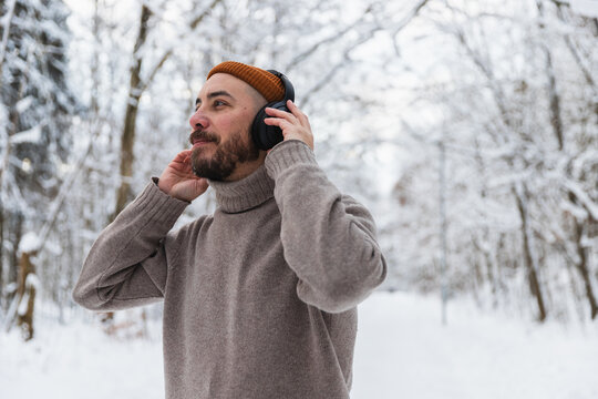 Man wearing headphones and using smartphone in snowy winter forest