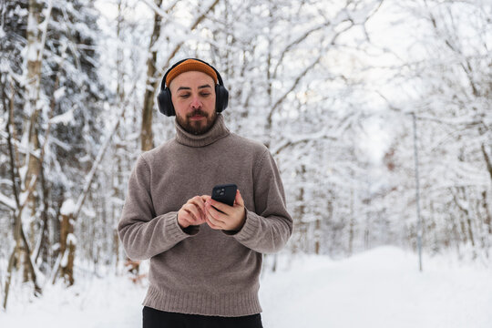 Man wearing headphones and using smartphone in snowy winter forest