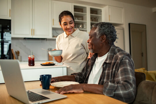 Caregiver serving breakfast to senior man in home kitchen