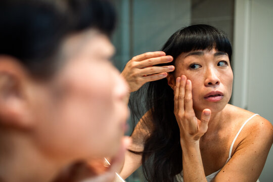 Woman examining facial skin in bathroom mirror