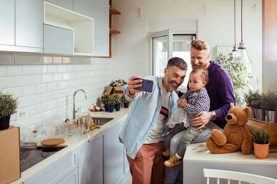 Two men taking selfie with toddler in new home kitchen