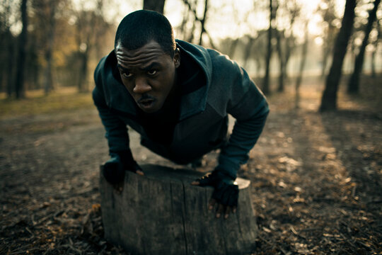 Young man doing incline push-ups on a tree stump in a forest park