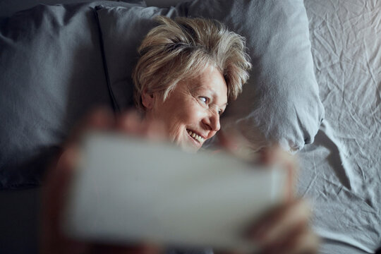 Smiling senior woman using smartphone in bed at home
