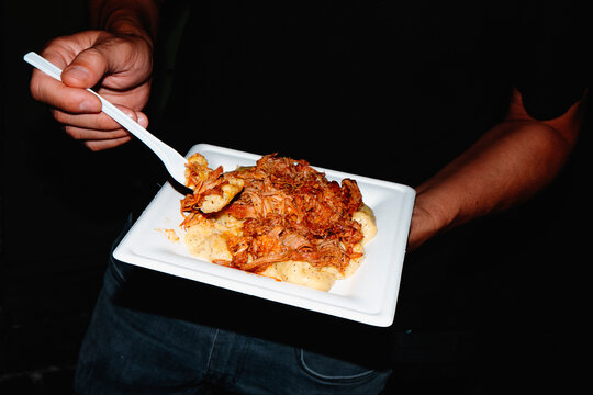 a man eating polenta with pulled pork from a street food plate