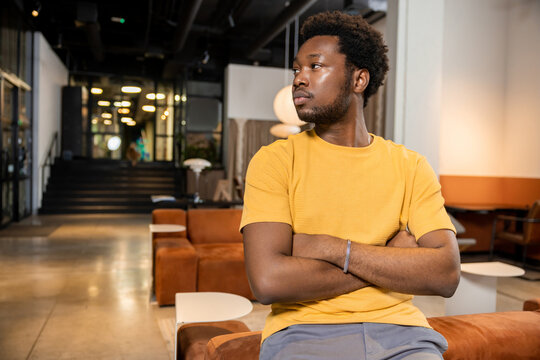 African American man sitting on sofa with arms crossed looking away in coworking space