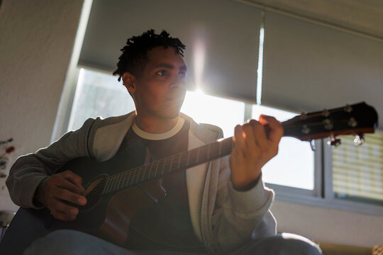 Musician playing acoustic guitar by window sunlight