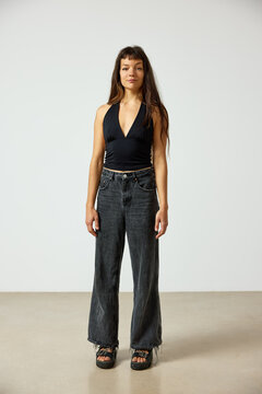 Model stands in studio wearing black top and wide jeans