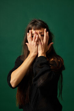 Young woman covering her face in front of green background