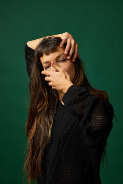 Woman poses with hands on face against green background