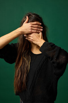 Person covering face with hands against a solid green background