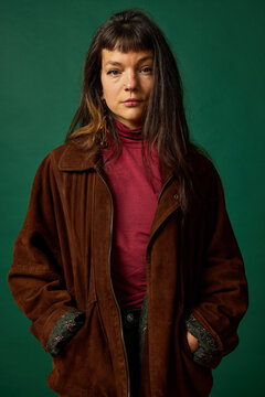 Model poses in brown jacket against green background in studio
