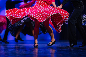 Latvian folk dancers in vibrant polka dot dresses performing traditional dance on stage with colorful lighting and dynamic movements © Raivo