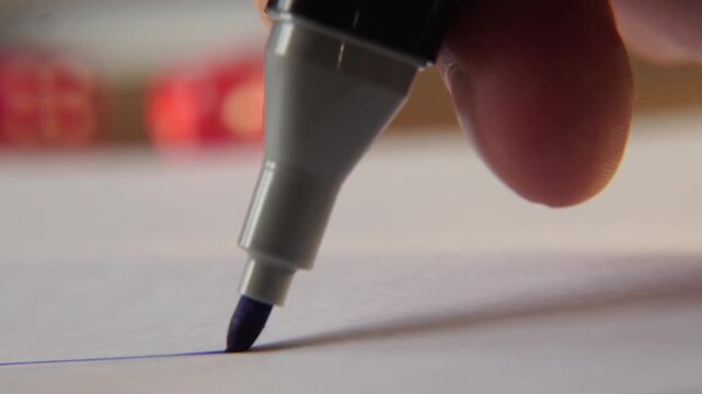 macro close up of person fingers holding blue marker and drawing a straight line on white paper with detailed tip of pen and ink texture