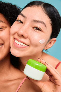 Smiling woman applying face cream with green container