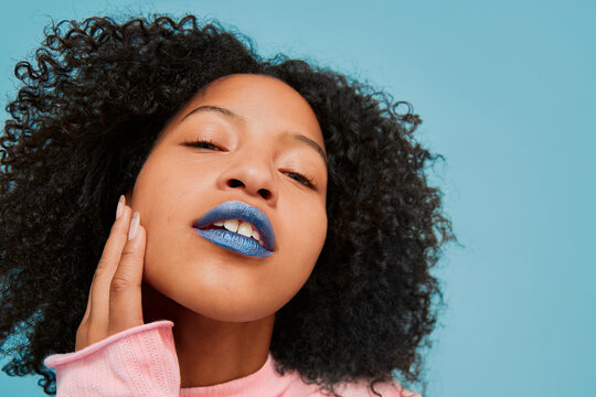 Portrait of a young Latina with curly hair and blue lipstick.