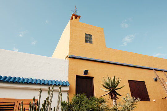 Yellow adobe building against blue sky with cactus plants