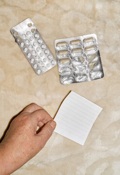 Hand holding blank note near pills blister packs at home