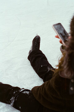Ice skater sitting on rink with phone  
