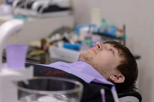 Male patient reclining in dental chair during oral examination with dental tools and equipment visible in the background