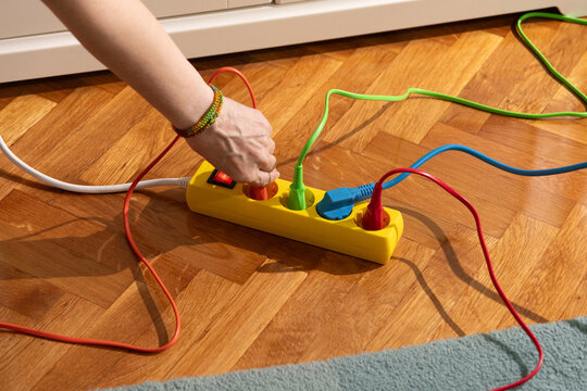 Hand Plugging Colorful Cord into Power Strip on Wooden Floor