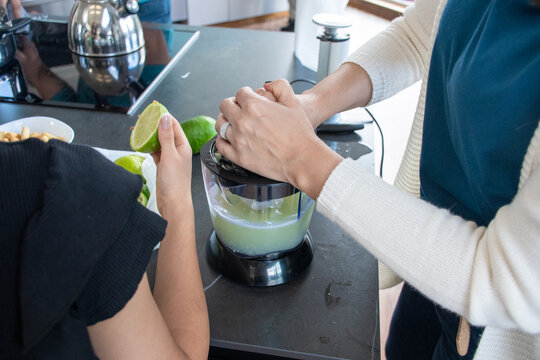 Women Preparing Lime Juice in Kitchen With Blender and Fresh Limes