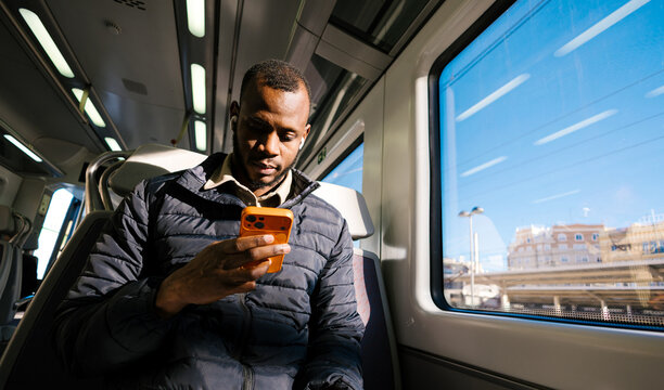 Black man commuting by train using phone with earbud