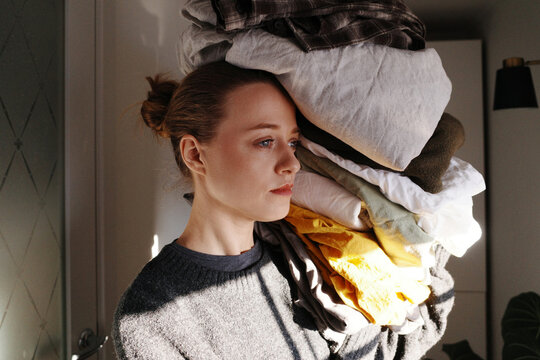 Woman burdened by large pile of laundry, feeling stressed