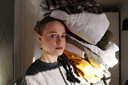 Woman carrying large pile of laundry exhausted from chores