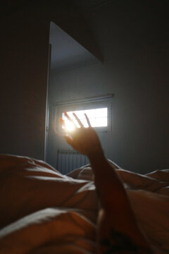Hand reaching for morning sun rays in bedroom