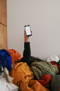 Hand holding smartphone emerging from laundry pile