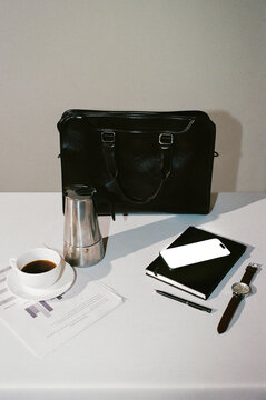 leather briefcase, coffee, moka pot, phone, and documents