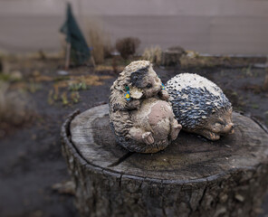 Obraz premium Vintage hedgehog garden statues with weathered paint on a wooden stump. Wabi-sabi garden decor