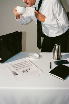 Man drinking coffee while adjusting tie before leaving
