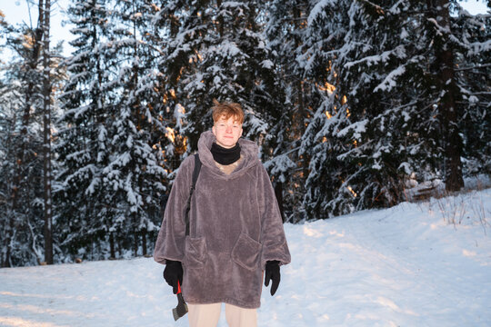 Man in Snowy Forest Wearing Large Coat and Holding Axe