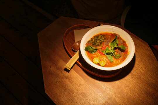 Bowl of soup with herbs and lime on a wooden table 