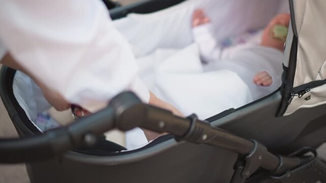White parent adjusting newborn in stroller, bassinet wrapped in white blanket, gentle hands smoothing fabric, closeup of canopy and handle, soft morning light, calm urban outing, tender caregiving