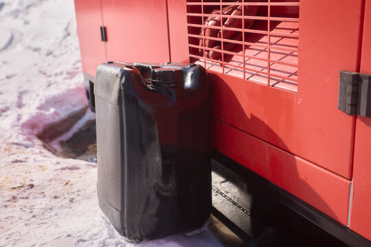 Equipment on snow. Scene showing fuel container against metal housing in winter setting. Rugged industrial equipment resting on snow with melting and salt stains visible