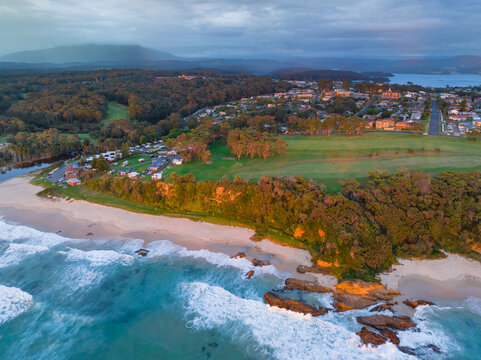 Golden light on waves and a rocky coastline below a golf course