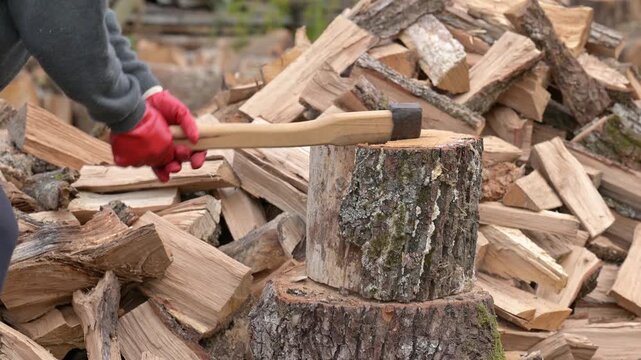 Man in red gloves chopping a wooden log with an axe. The process of fuel harvesting and active physical labor outdoors as a symbol of winter preparation and coziness