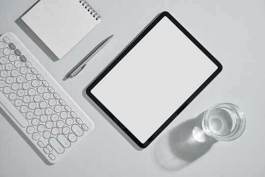 Minimalist workspace with tablet, keyboard, and water glass on white