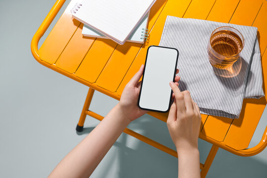 Hands holding a smartphone with a blank screen on a yellow table.